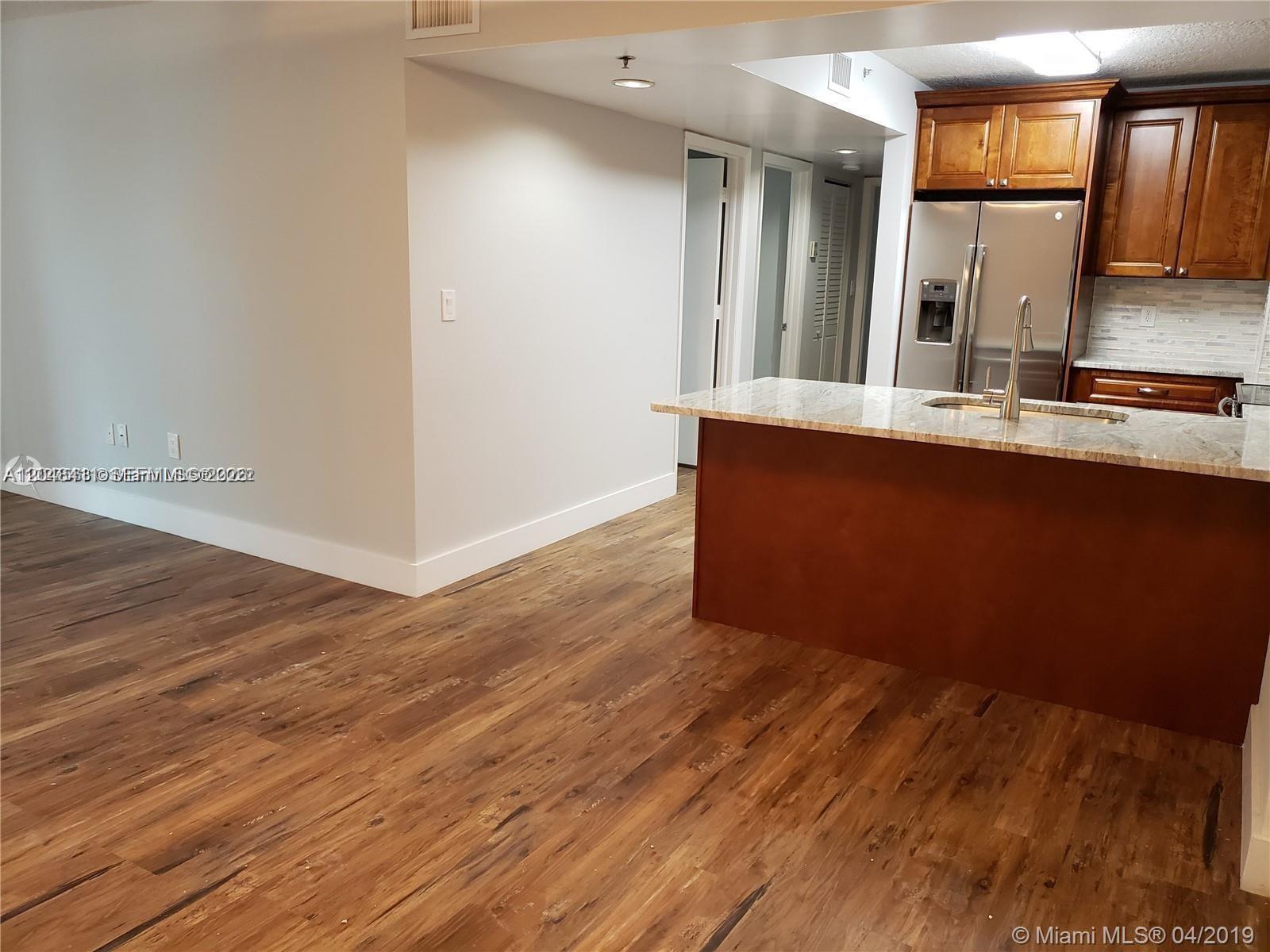 A kitchen with wood cabinets and a granite island overlooks a wood-floored living area — 104 SW 9th St # 304, Miami FL 33130, MIAMI, FL