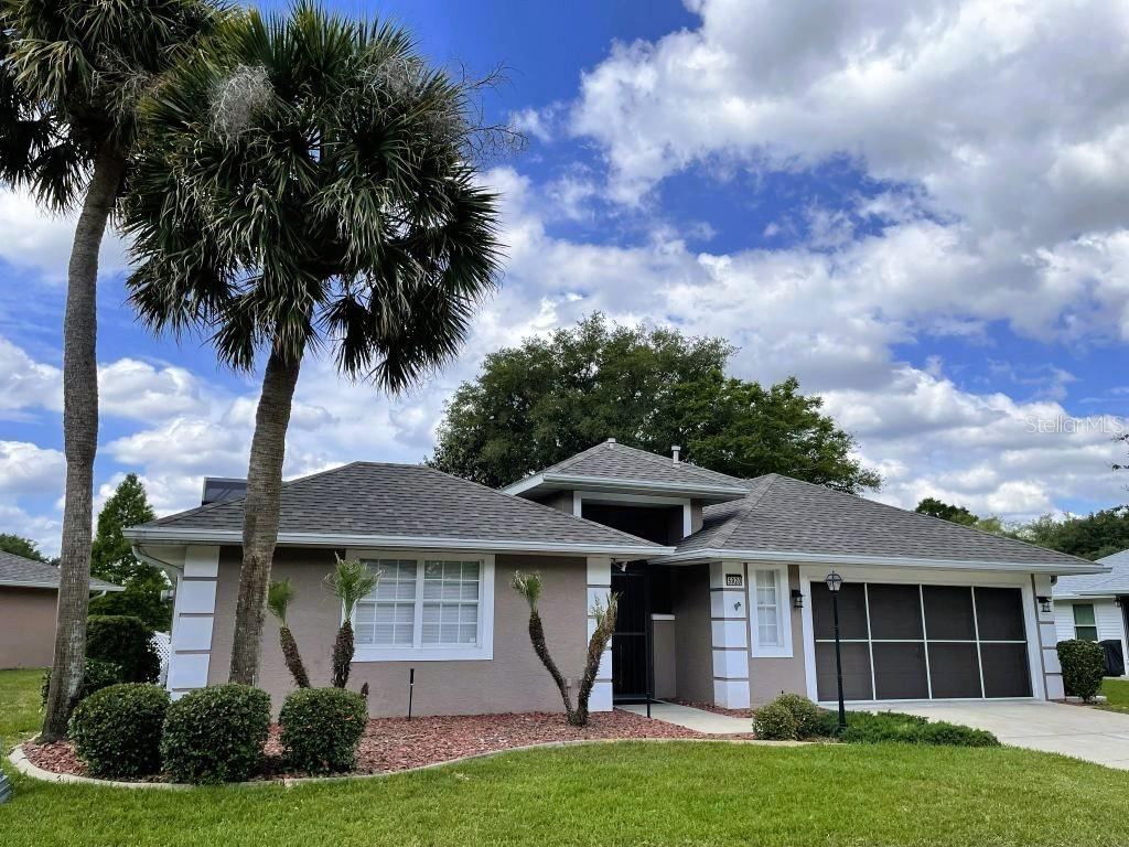 A single-story house with a gray roof, tan stucco exterior, and a palm tree — 5920 BAG PIPE PLACE, LEESBURG, FL