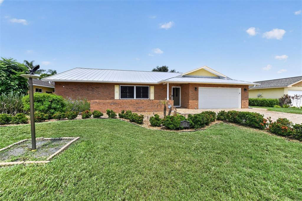 A single-story brick house with a metal roof, a two-car garage, and a landscaped lawn — 212 68TH STREET NW, BRADENTON, FL