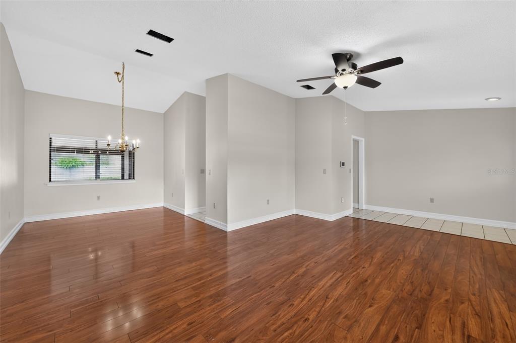 An empty room with wood flooring, a ceiling fan, and a dining area chandelier — 212 68TH STREET NW, BRADENTON, FL
