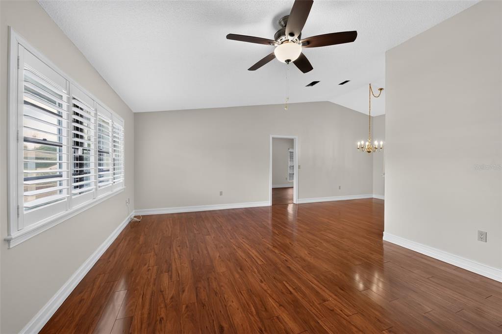 An empty room with hardwood floors, a ceiling fan, and white plantation shutters — 212 68TH STREET NW, BRADENTON, FL