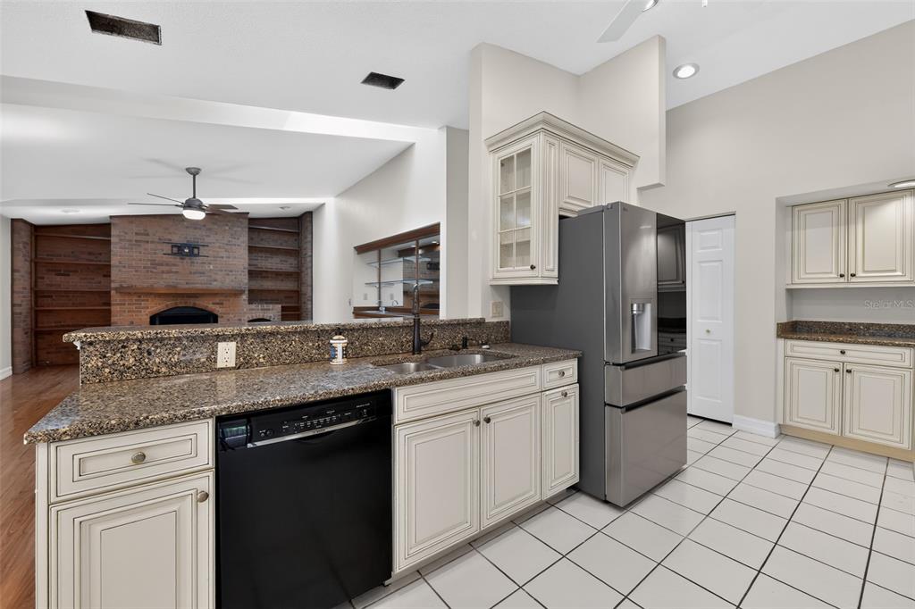 A kitchen features cream-colored cabinets, granite countertops, a black dishwasher, and a stainless refrigerator — 212 68TH STREET NW, BRADENTON, FL