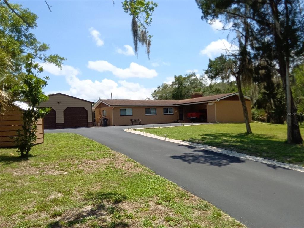 A tan ranch-style house with a detached garage and a long asphalt driveway — 758 BUFFALO ROAD, TITUSVILLE, FL