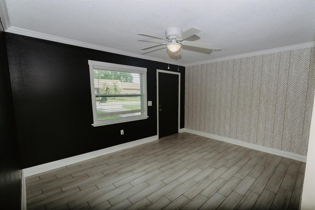 A bedroom features black walls, a patterned accent wall, light wood-look tile flooring, and a ceiling fan — 2040 WOODBRIAR LOOP S, LAKELAND, FL