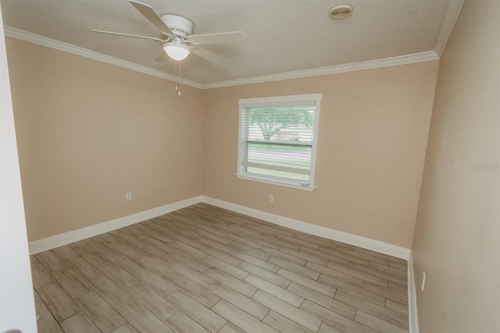 An empty bedroom features light tan walls, wood-look tile flooring, and a ceiling fan — 2040 WOODBRIAR LOOP S, LAKELAND, FL