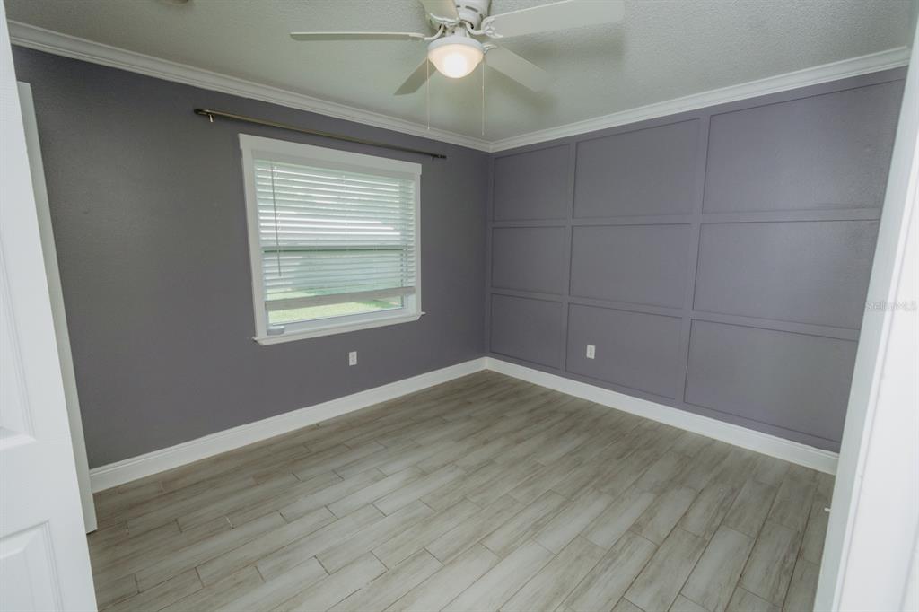 An empty bedroom features gray walls with wainscoting, a ceiling fan, and wood-look tile flooring — 2040 WOODBRIAR LOOP S, LAKELAND, FL