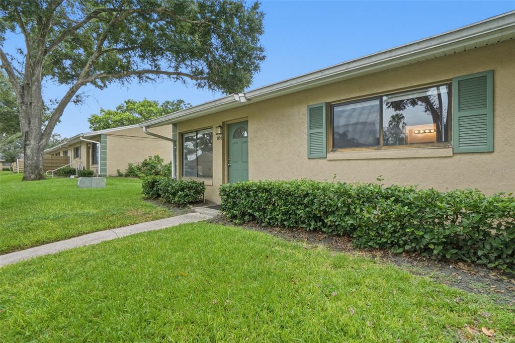 A single-story tan stucco building with a green door, shutters, and a front lawn — 220 CHEROKEE COURT UNIT 104, ALTAMONTE SPRINGS, FL