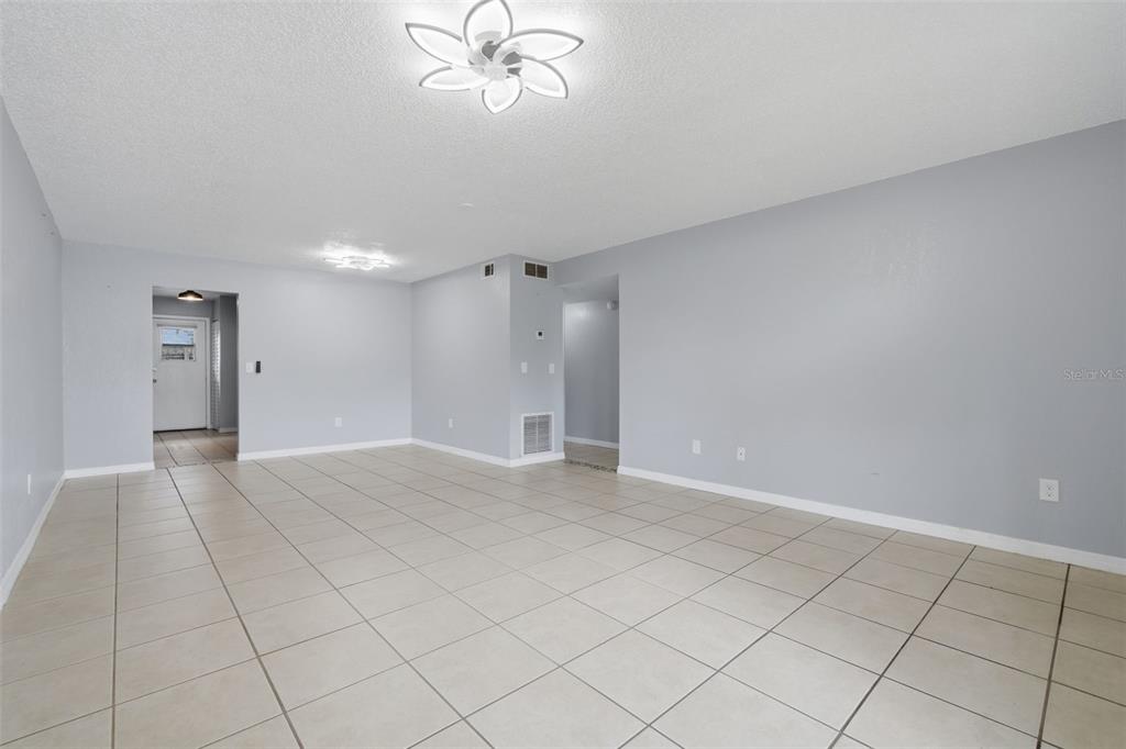 An empty room features light gray walls, large beige floor tiles, and two modern light fixtures — 220 CHEROKEE COURT UNIT 104, ALTAMONTE SPRINGS, FL