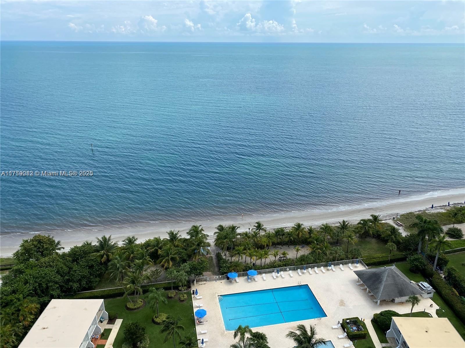 An aerial view shows a swimming pool, palm trees, and a sandy beach by the ocean — 881 Ocean Dr # 22F, Key Biscayne FL 33149, KEY BISCAYNE, FL