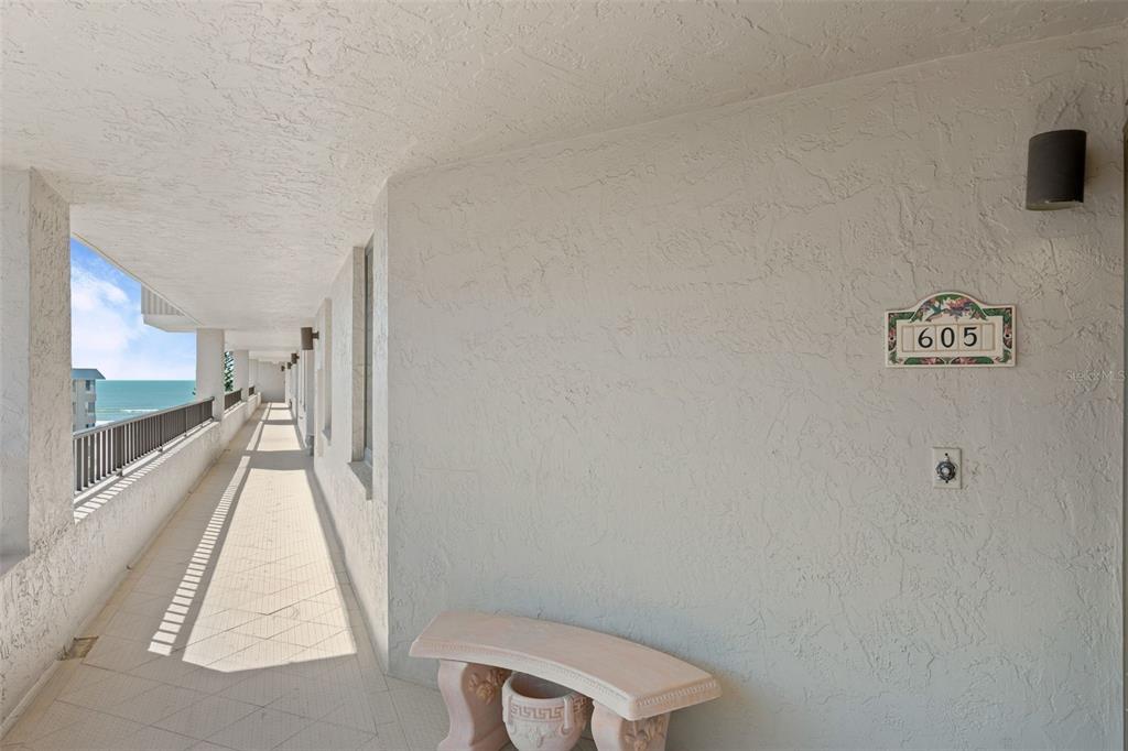 An outdoor balcony walkway features a stone bench, a unit number sign, and ocean views — 5880 MIDNIGHT PASS ROAD UNIT 605, SARASOTA, FL