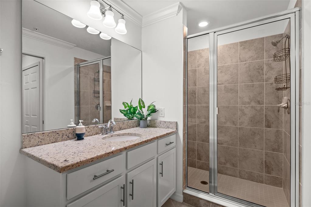 A bathroom features a granite vanity, gray cabinets, and a glass-enclosed tiled shower — 43040 GREENWAY BOULEVARD UNIT 536, PUNTA GORDA, FL