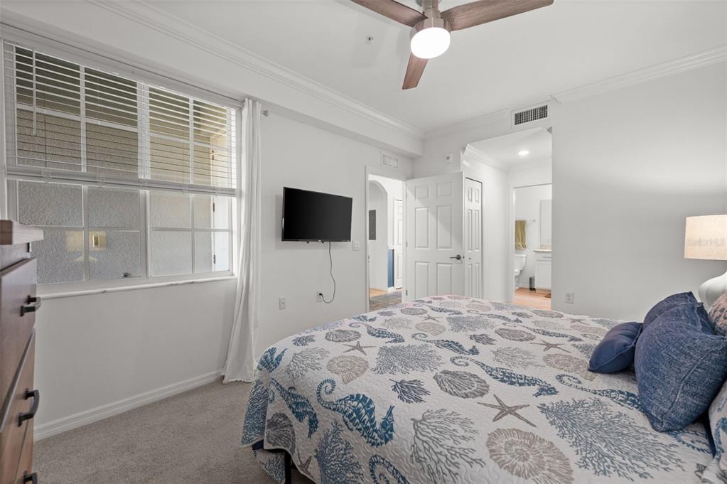 A bedroom features a bed with a seashell-patterned quilt, a wall-mounted television, and a window — 43040 GREENWAY BOULEVARD UNIT 536, PUNTA GORDA, FL