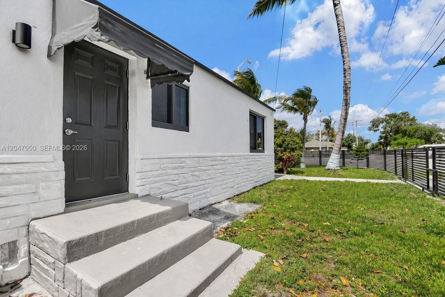 A white house exterior features a dark door, concrete steps, and a fenced grassy yard — 1102 NW 103rd St, Miami FL 33150, MIAMI, FL