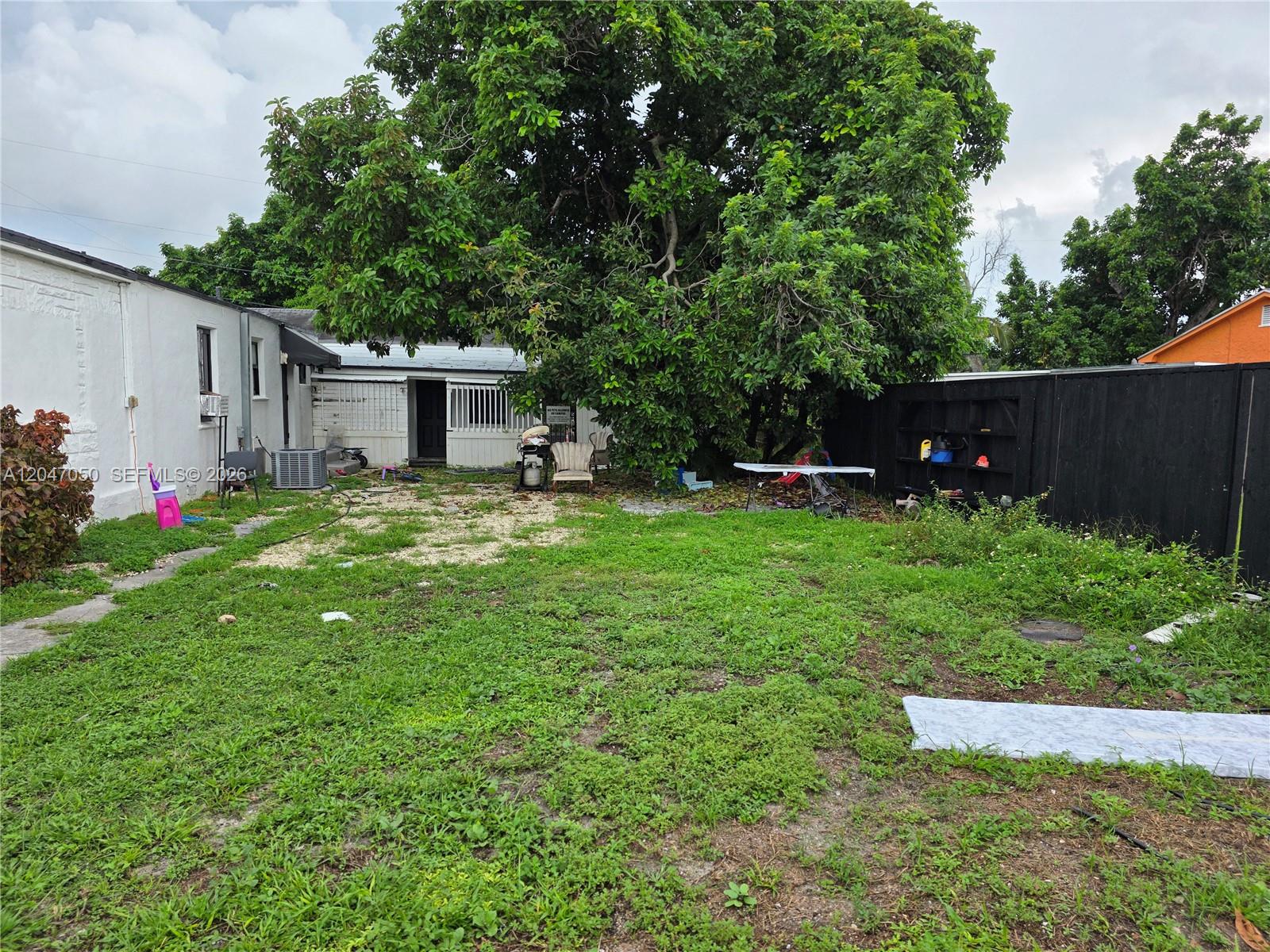 A backyard features a large tree, a white house, a black fence, and patchy grass — 1102 NW 103rd St, Miami FL 33150, MIAMI, FL