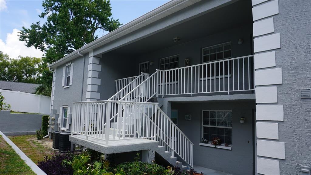 A two-story gray building features white railings, a staircase, and white corner accents — 12141 SPARTAN WAY UNIT 204, HUDSON, FL