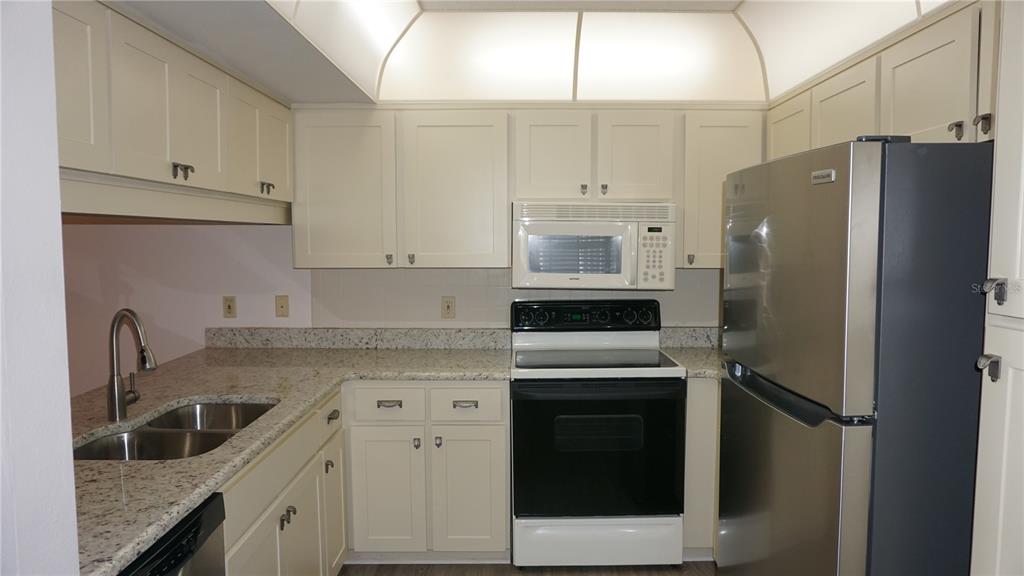 A kitchen with cream cabinets, granite countertops, and stainless steel appliances — 12141 SPARTAN WAY UNIT 204, HUDSON, FL