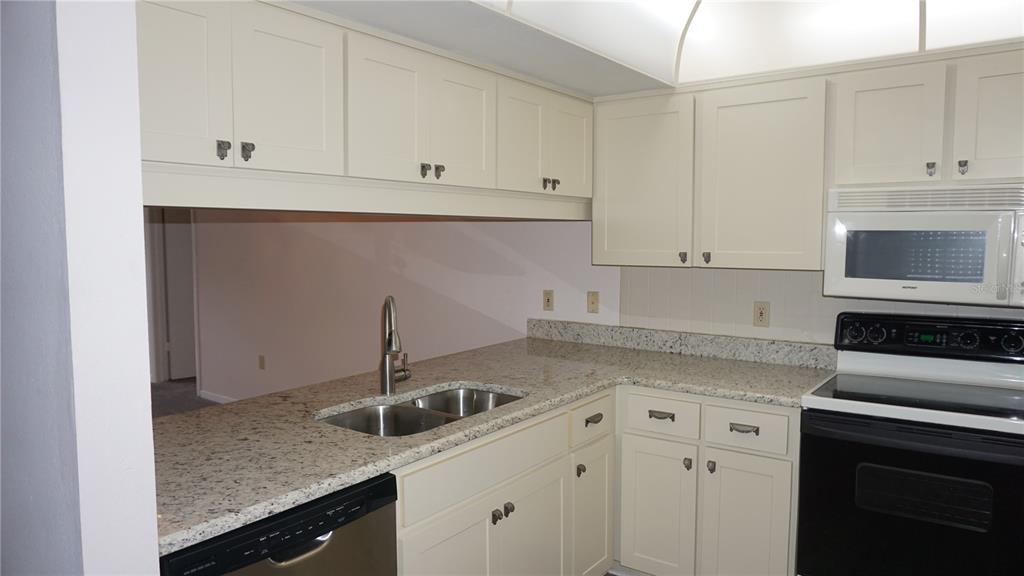 A kitchen features off-white cabinets, granite countertops, a stainless steel sink, and black appliances — 12141 SPARTAN WAY UNIT 204, HUDSON, FL