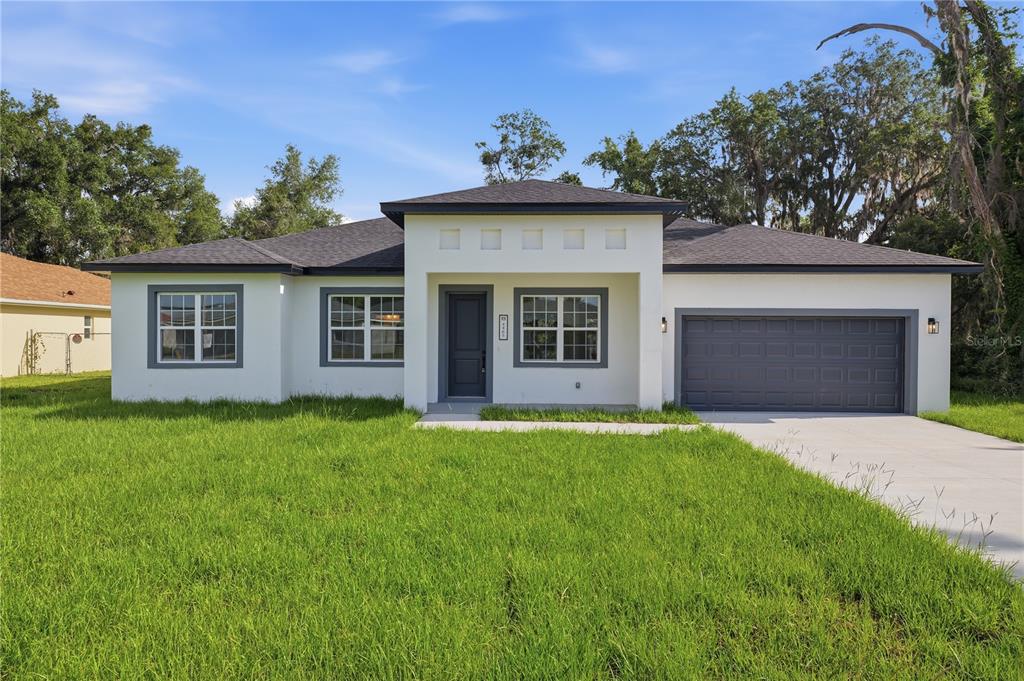 A single-story white house with a dark gray garage door and a flat roof section — 4465 SW 132ND STREET, OCALA, FL