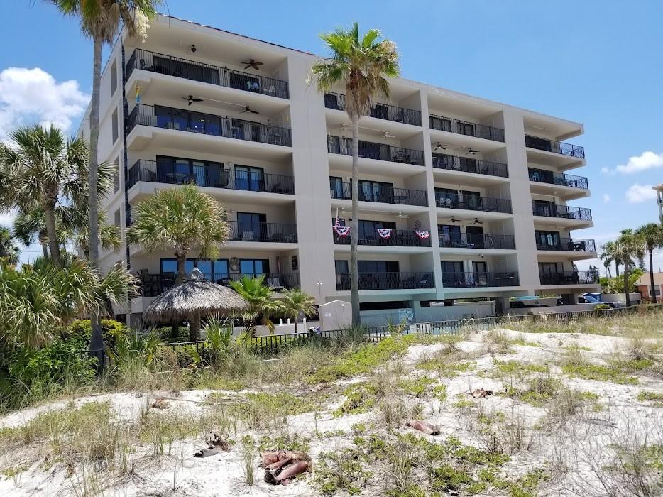 A multi-story beachfront condominium building features balconies overlooking a sandy dune area with palm trees — 13650 GULF BOULEVARD UNIT 304, MADEIRA BEACH, FL