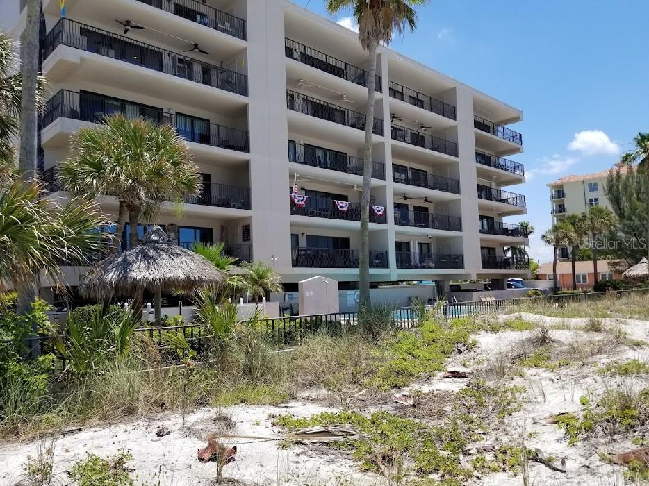 A multi-story beachfront condominium building features balconies and a thatched-roof tiki hut on sand — 13650 GULF BOULEVARD UNIT 304, MADEIRA BEACH, FL