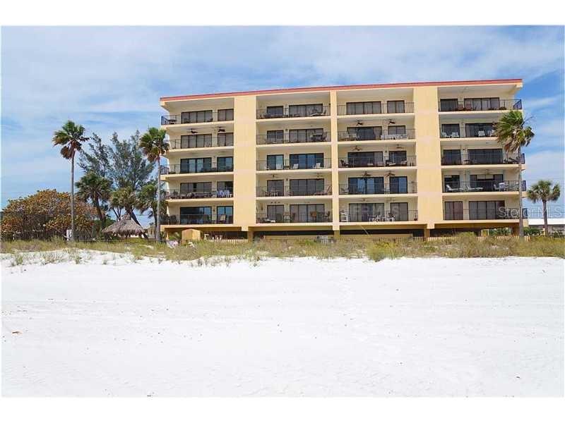 A multi-story apartment building with balconies faces a white sand beach with palm trees — 13650 GULF BOULEVARD UNIT 304, MADEIRA BEACH, FL