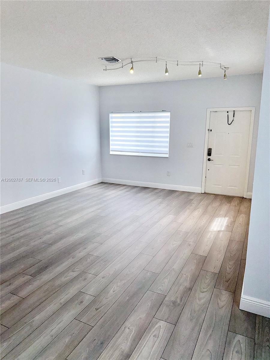 An empty room features light gray walls, wood-look flooring, a window with blinds, and track lighting — 1704 SW 101st Ter, Miramar FL 33025, MIRAMAR, FL