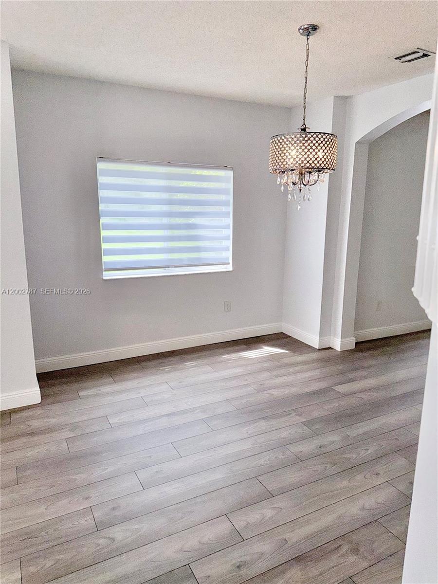 A dining area features light gray walls, wood-look flooring, and a decorative crystal chandelier — 1704 SW 101st Ter, Miramar FL 33025, MIRAMAR, FL