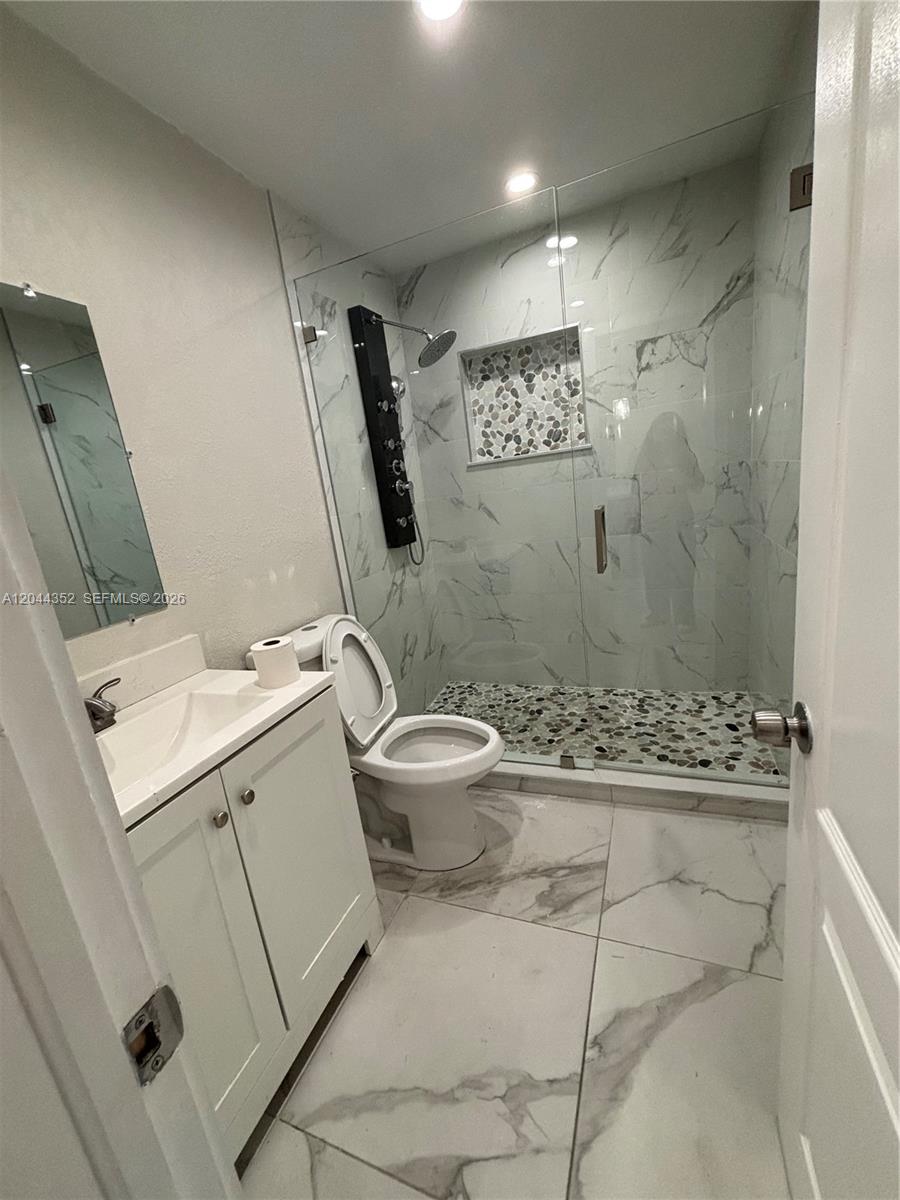 A bathroom features a white vanity, a toilet, and a glass-enclosed shower with pebble flooring — 5011 SW 5th St # 0, Miami FL 33134, MIAMI, FL