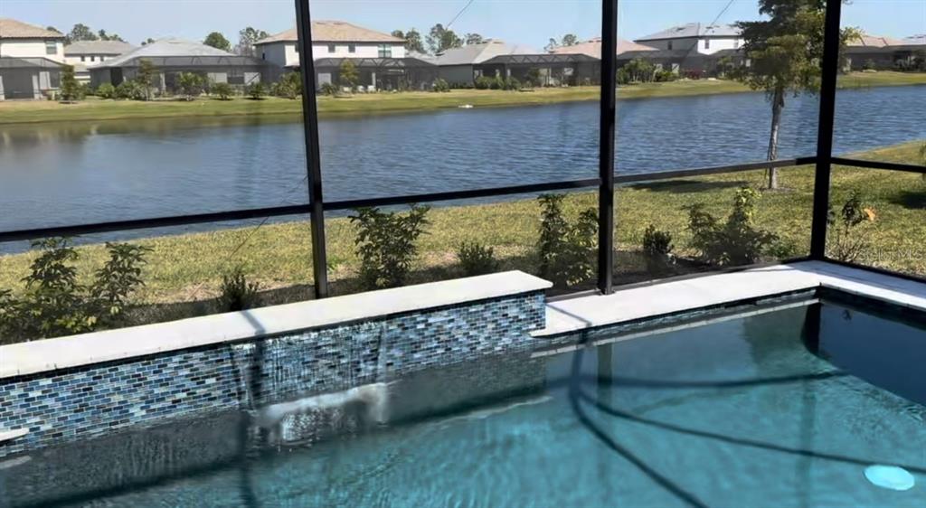 A screened-in patio features a rectangular swimming pool with a water feature and lake view — 4967 SEAFOAM TRAIL, BRADENTON, FL