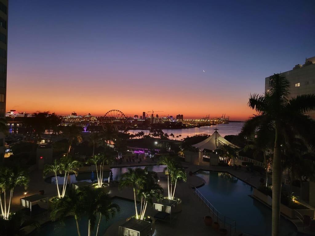 An elevated view of a swimming pool area at dusk with a city skyline background — 244 Biscayne Boulevard # 2805, Miami FL 33132, MIAMI, FL