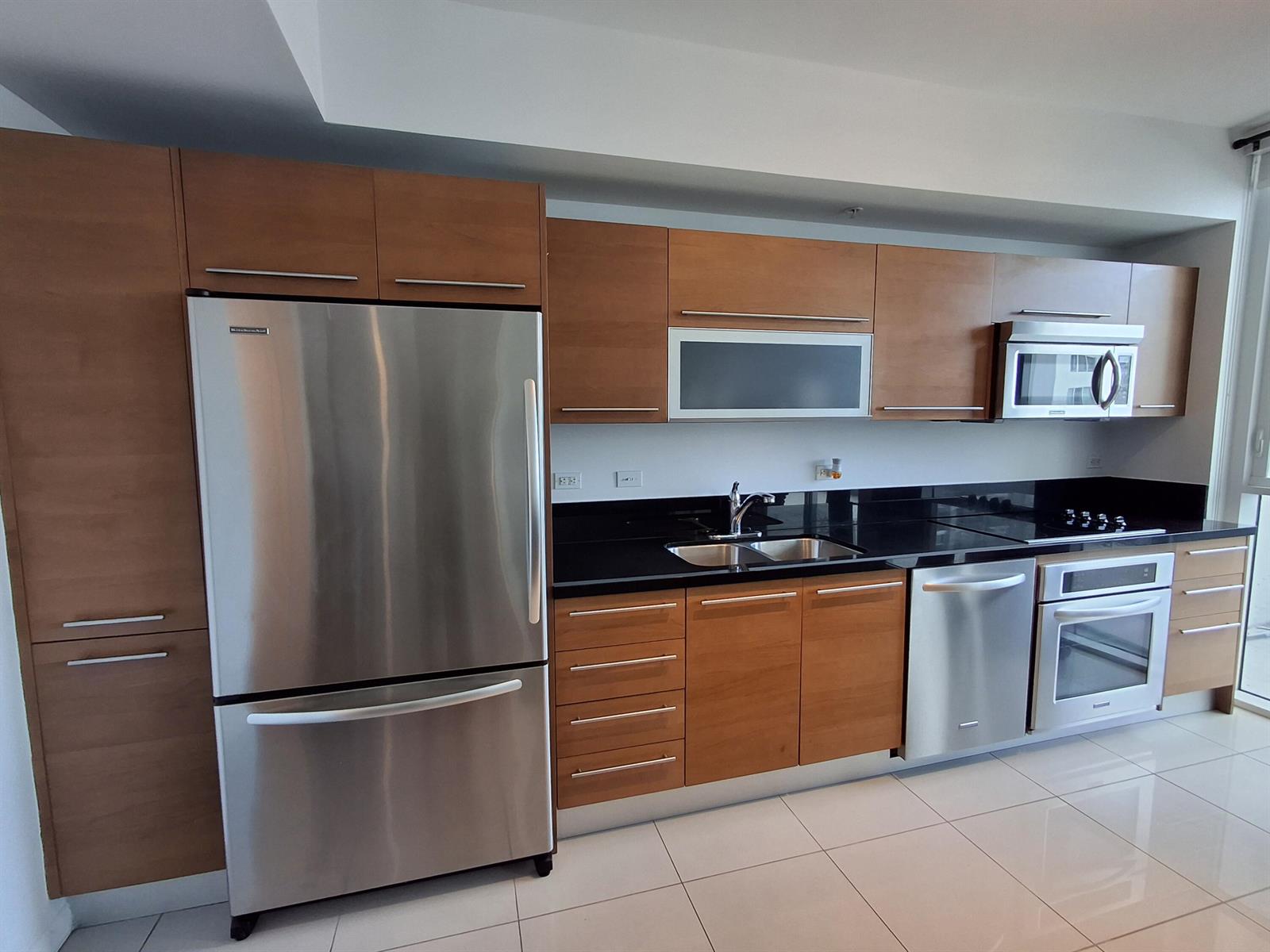A modern kitchen features wood cabinets, stainless steel appliances, and black countertops on tile flooring — 244 Biscayne Boulevard # 2805, Miami FL 33132, MIAMI, FL