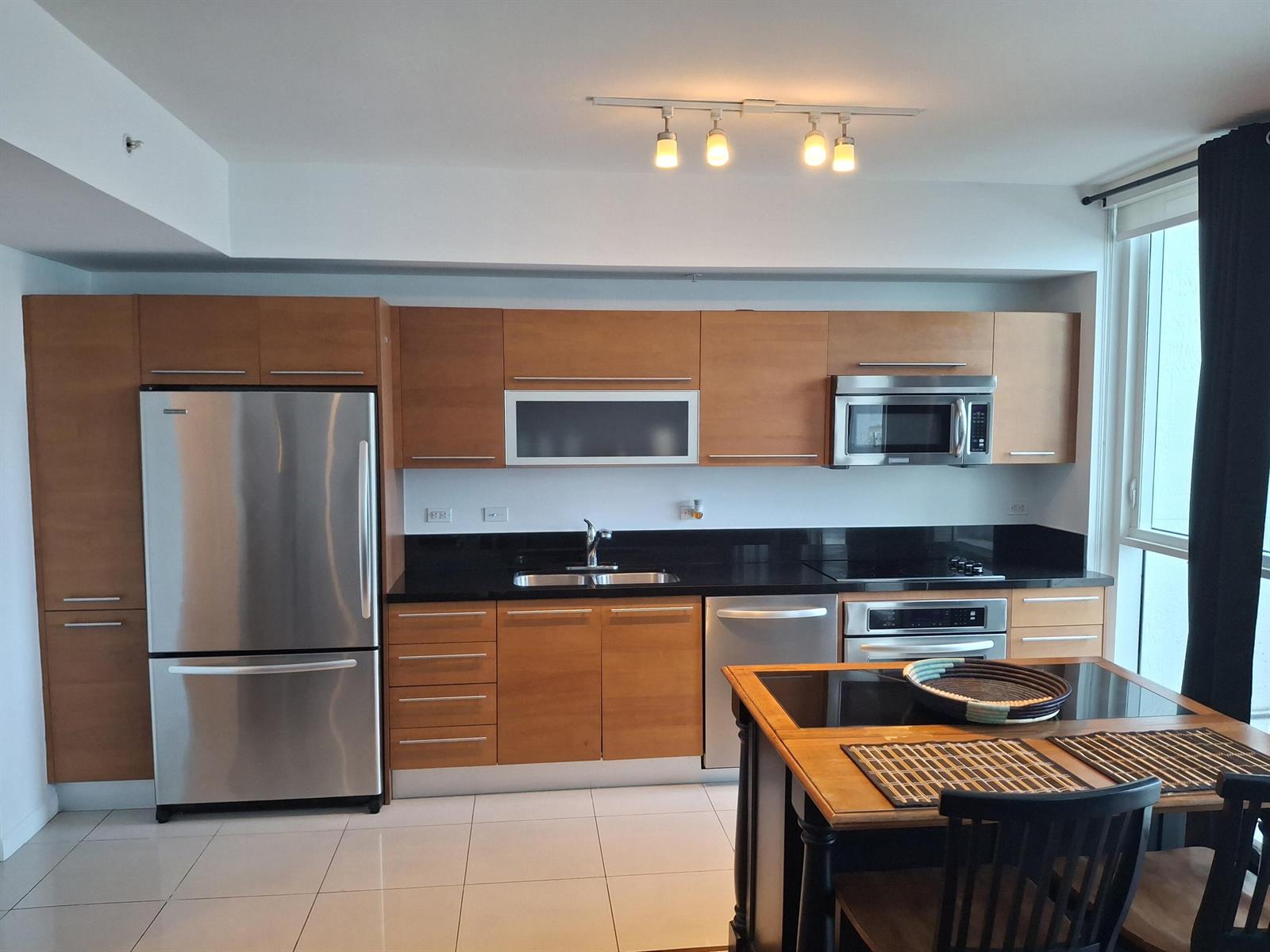 A modern kitchen features wood cabinets, stainless steel appliances, black countertops, and a dining island — 244 Biscayne Boulevard # 2805, Miami FL 33132, MIAMI, FL