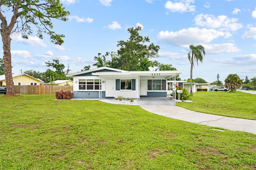 A single-story house with a white exterior, blue accents, and a carport on a lawn — 2237 2ND AVENUE E, BRADENTON, FL