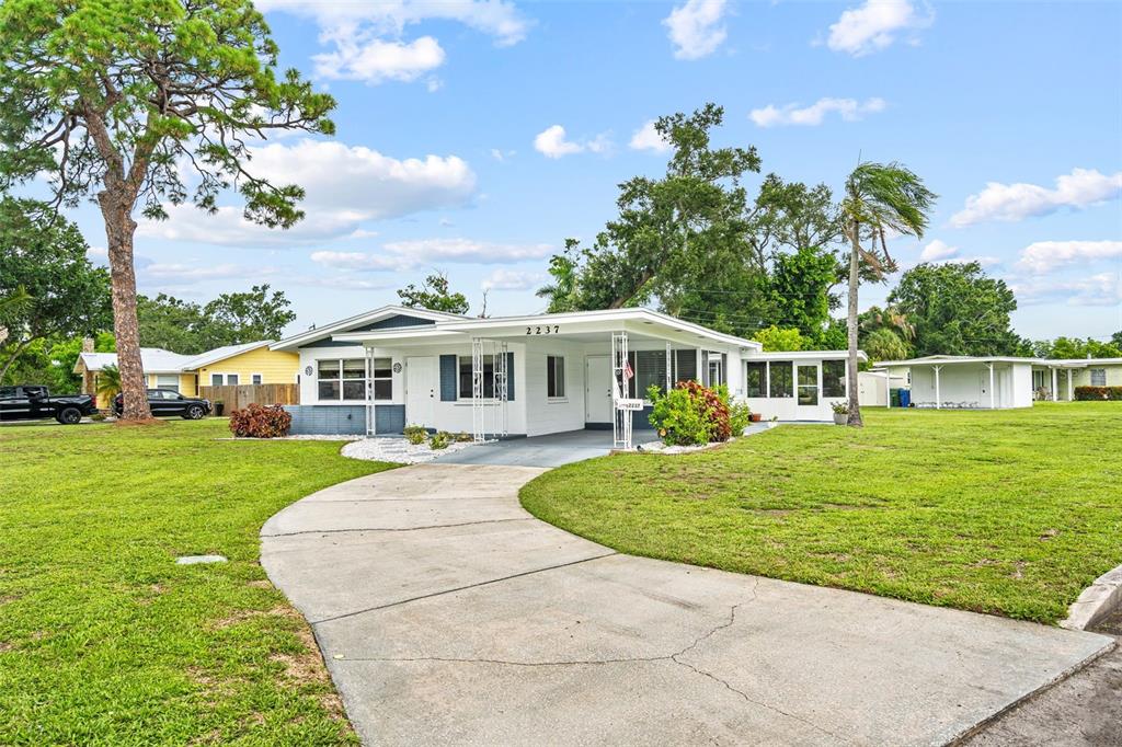 A single-story white house with a carport and a curved concrete driveway sits on grass — 2237 2ND AVENUE E, BRADENTON, FL