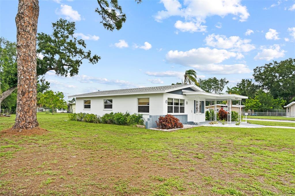 A white single-story house with a carport sits on a large, grassy lot — 2237 2ND AVENUE E, BRADENTON, FL