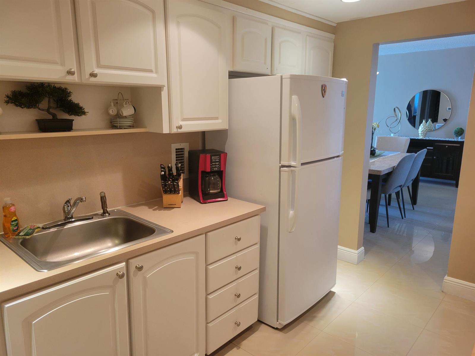 A kitchen features white cabinets, a stainless steel sink, a white refrigerator, and tile flooring — 3901 S Ocean Drive # 12t, Hollywood FL 33019, HOLLYWOOD, FL