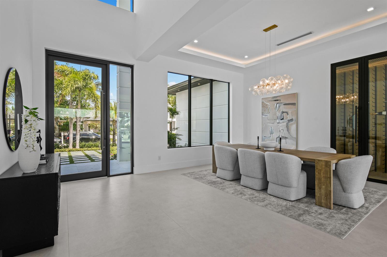 A modern dining room features a wooden table, upholstered chairs, and large floor-to-ceiling windows — 2408 Azure Circle, Palm Beach Gardens FL 33410, PALM BEACH GARDENS, FL