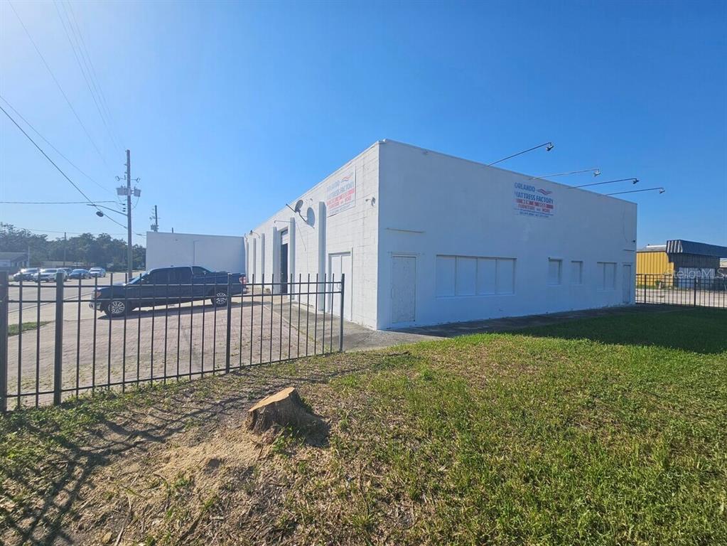 A white, single-story commercial building with a fenced parking lot under a clear blue sky — 2698 S ORANGE BLOSSOM TRAIL, ORLANDO, FL