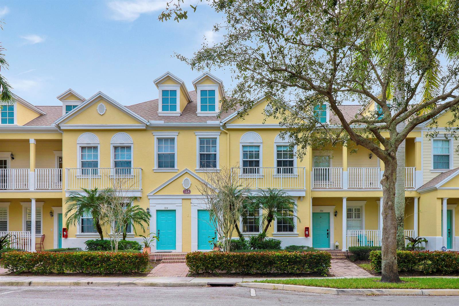 A row of yellow townhouses with teal doors, white railings, and a large tree in front — 118 Seagrape Drive # 105, Jupiter FL 33458, JUPITER, FL