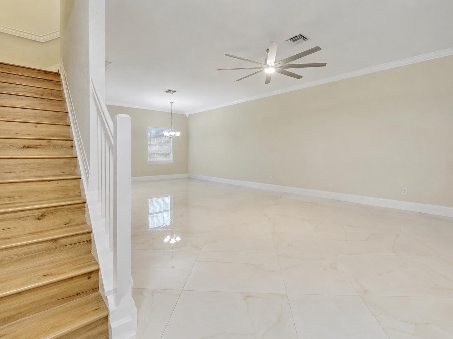 An open living area features large light-colored floor tiles, a ceiling fan, and wooden stairs — 118 Seagrape Drive # 105, Jupiter FL 33458, JUPITER, FL