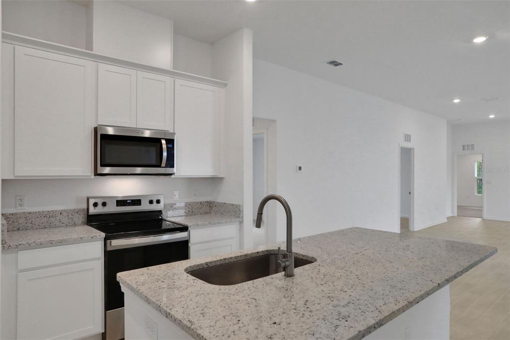 A kitchen features white cabinets, granite countertops, a stainless steel microwave, and a center island — 3889 HOLSTEIN WAY, GREEN COVE SPRINGS, FL