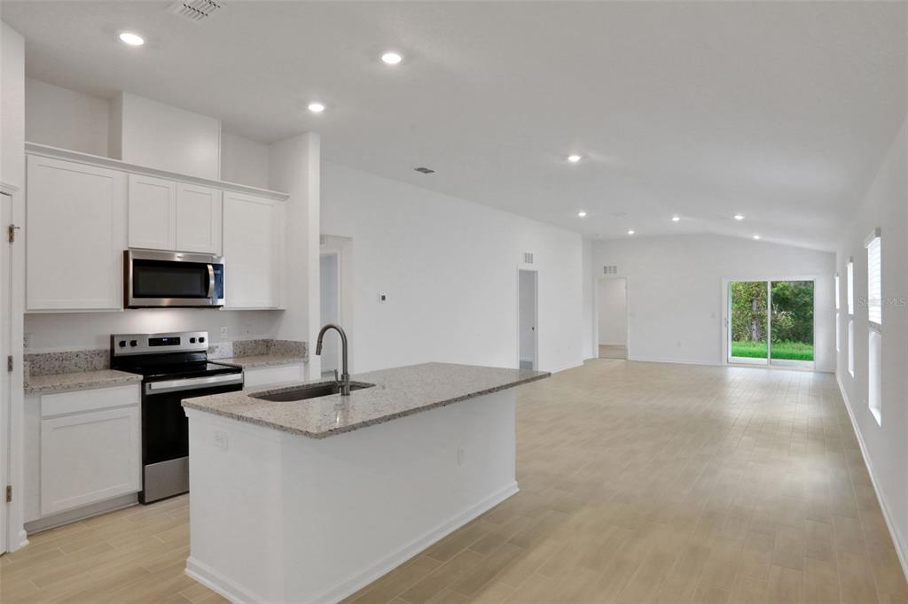 A kitchen with white cabinets and granite countertops opens into a spacious, light-filled living area — 3889 HOLSTEIN WAY, GREEN COVE SPRINGS, FL