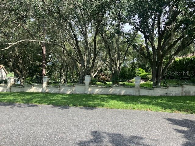 A low concrete wall with stone pillars borders a grassy yard shaded by large trees — 116 W MAGNOLIA AVENUE, HOWEY IN THE HILLS, FL