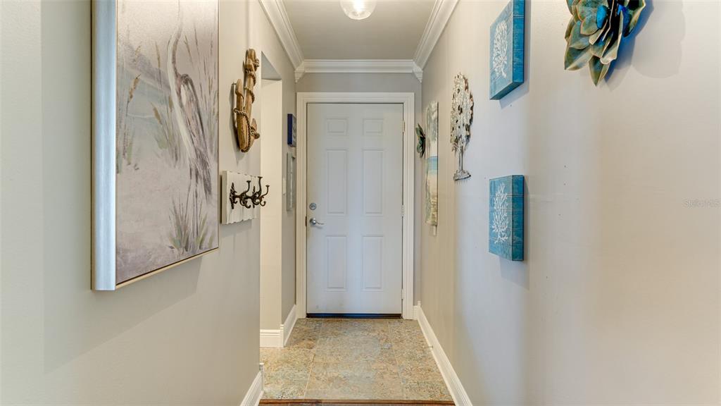 A hallway with tiled flooring, light gray walls, and coastal-themed wall decor leads to a door — 3276 LAKE BAYSHORE DRIVE N UNIT O-517, BRADENTON, FL