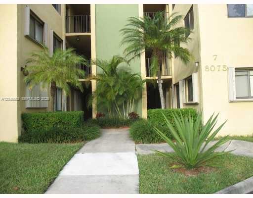 A concrete walkway leads to the entrance of a multi-story apartment building with palm trees — 8075 SW 107th Ave # 305, Miami FL 33173, MIAMI, FL