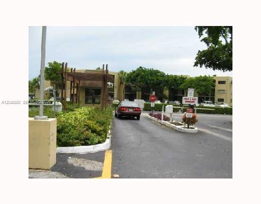 A car drives through the gated entrance of a multi-story apartment complex with lush landscaping — 8075 SW 107th Ave # 305, Miami FL 33173, MIAMI, FL