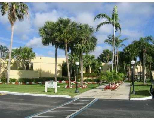 A paved walkway leads toward a yellow building surrounded by palm trees and landscaping — 8075 SW 107th Ave # 305, Miami FL 33173, MIAMI, FL