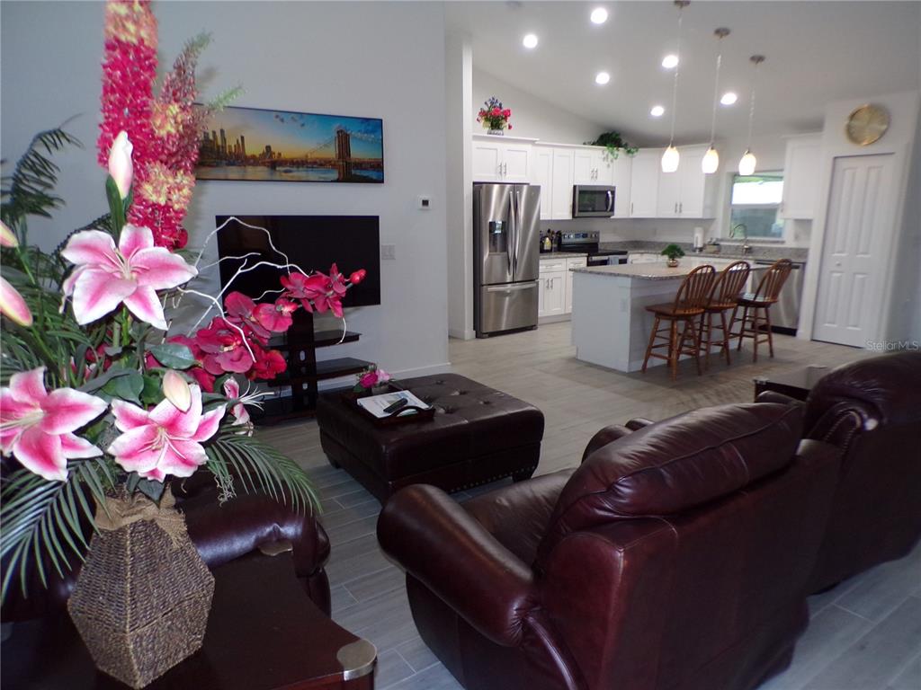 A living room with leather furniture opens into a kitchen featuring white cabinets and an island — 326 MILLPORT STREET NW, PORT CHARLOTTE, FL