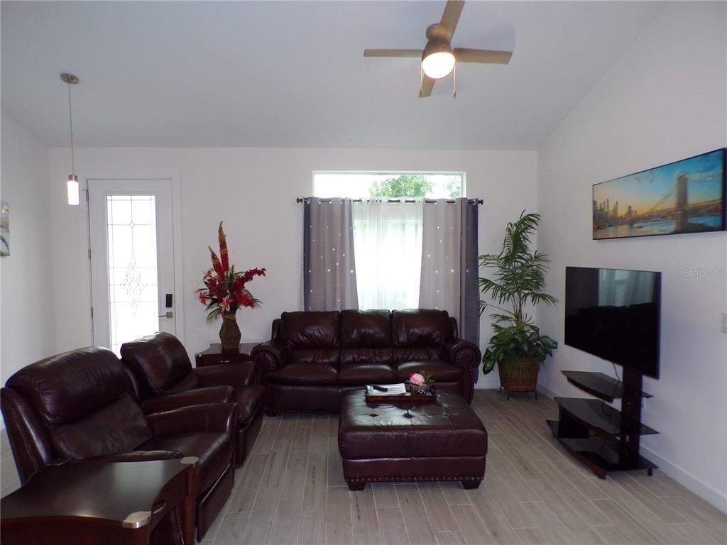 A living room features brown leather furniture, a television, and light-colored tile flooring — 326 MILLPORT STREET NW, PORT CHARLOTTE, FL