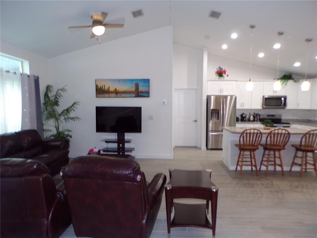 An open-concept living room and kitchen featuring leather furniture, a television, and a breakfast bar — 326 MILLPORT STREET NW, PORT CHARLOTTE, FL